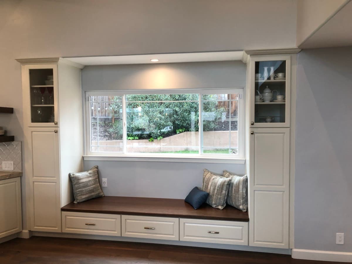 Floor-to-ceiling built-in cabinetry framing a window seat, flanked by tall glass-front display towers