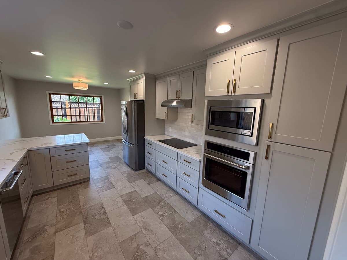 Light-gray shaker kitchen with a stacked wall-oven column, drawer-stack base cabinets, and brass pulls