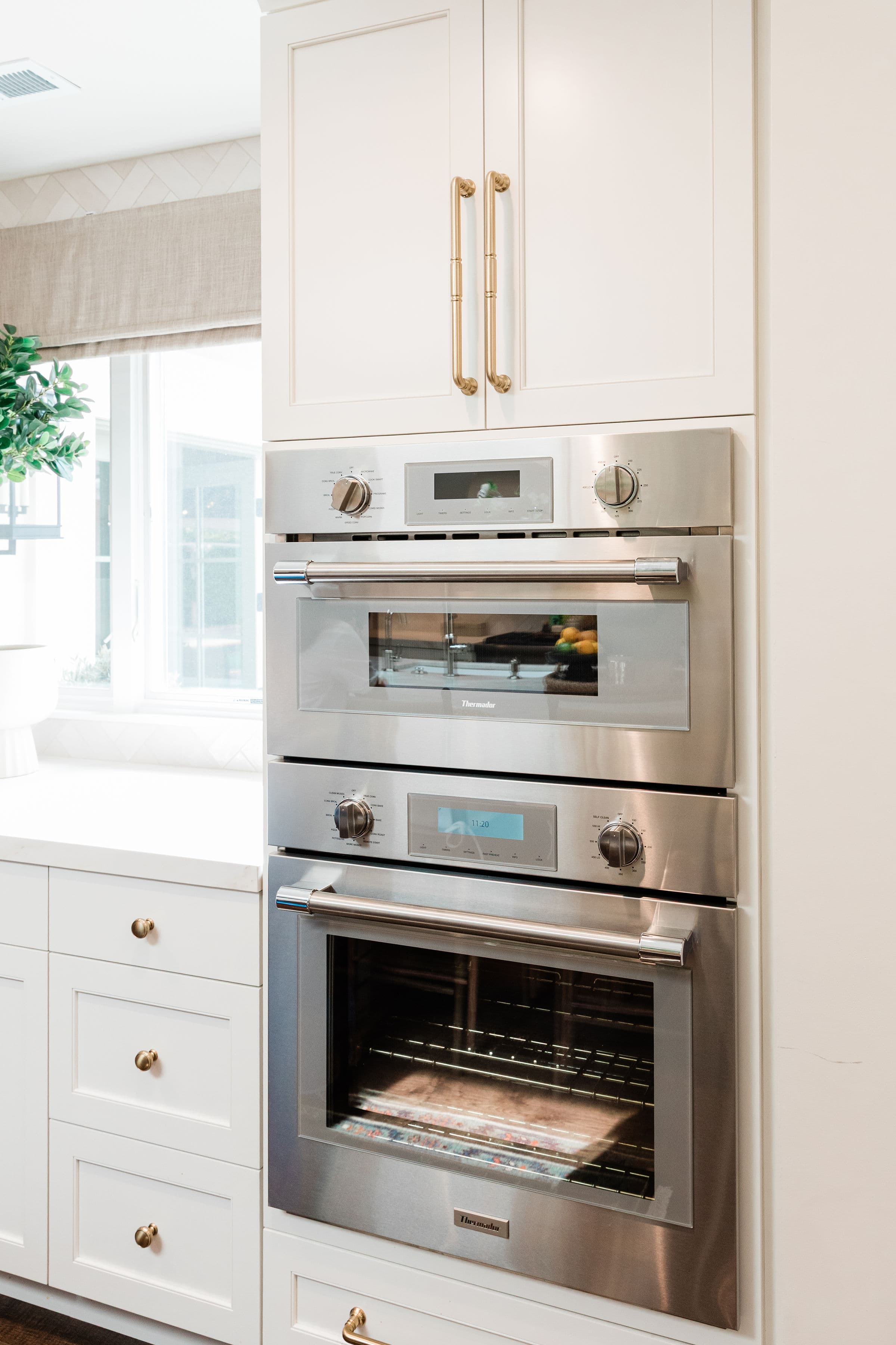 Detail of crisp white shaker cabinetry surrounding stacked double wall ovens with brass cup and bar pulls