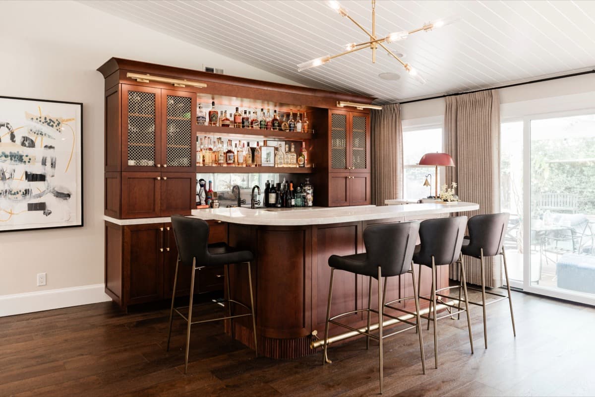 Full-height walnut wet bar with antique-brass metal-grille glass-front cabinets, a mirrored back, and a fluted curved base